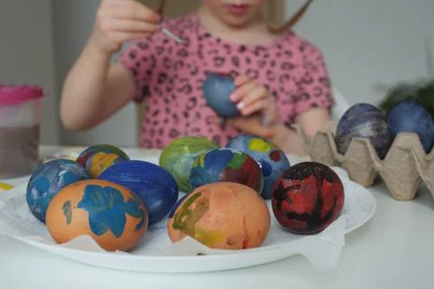 Painted Easter eggs by a child on a white plate and a girl in a pink dress in Stock Photos