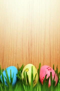 Painted Easter eggs in a green grass on a wooden background. Stock Photos