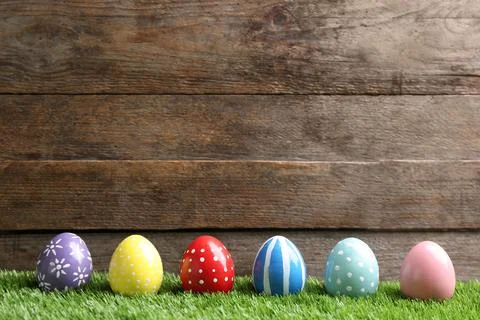 Painted Easter eggs on green grass against wooden background, space for text Foto stock