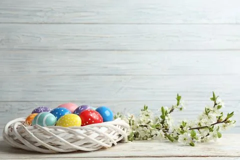 Painted Easter eggs in nest and blossoming branches on table. Space for text Stock Photos