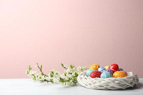 Painted Easter eggs in nest and blossoming branches on table against color ba Stock Photos