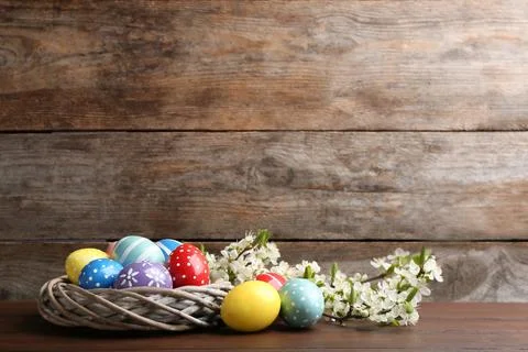 Painted Easter eggs in nest and blossoming branches on table against color ba Stock Photos