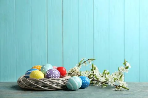 Painted Easter eggs in nest and blossoming branches on table against color ba Stock Photos