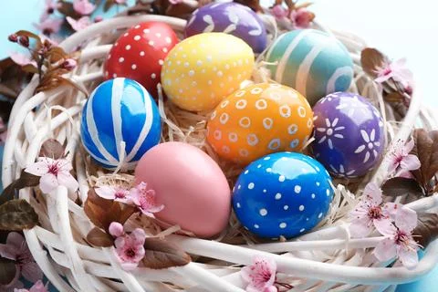 Painted Easter eggs in nest with flowers on color background, closeup Foto stock