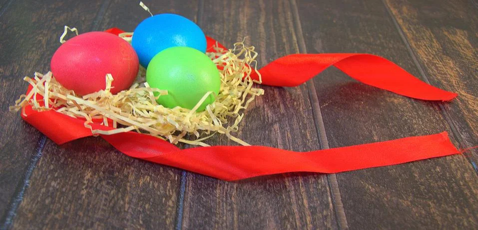 Painted Easter eggs in a nest of straw on a scarlet ribbon lie on a wooden ta Stock Photos
