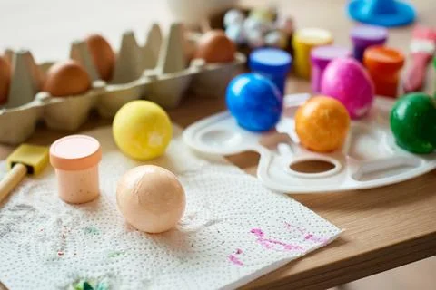 Painted Easter eggs with paints and palette on wooden table Stock Photos