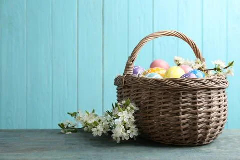 Painted Easter eggs in wicker basket and blossoming branches on table against Stock Photos