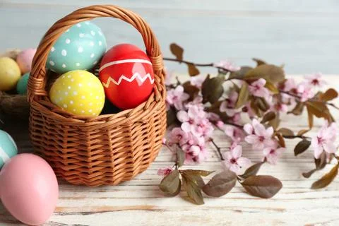 Painted Easter eggs in wicker basket and blossoming branches on wooden table Stock Photos