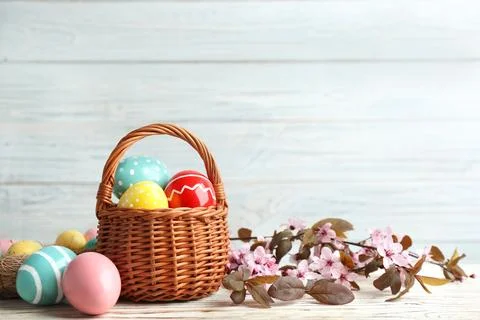 Painted Easter eggs in wicker basket and blossoming branches on table. Space  Stock Photos