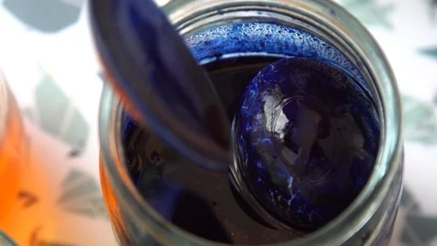 Painted egg in a jar of blue paint. spoon with egg dipped in liquid paint Stock Footage 127958264