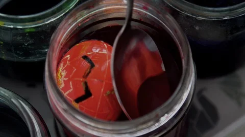 Painted egg in a jar of red  paint. spoon with egg dipped in liquid paint Stock Footage 127958292