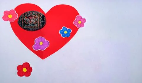 Painted egg lying on a red heart and painted flowers. Stock Photos