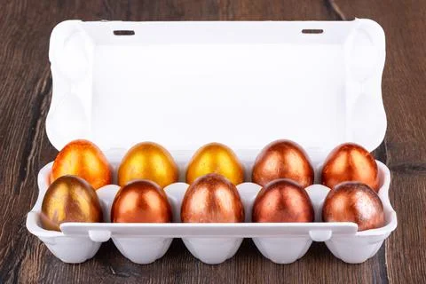 Painted in gold and bronze Easter eggs in a white plastic package on a wooden Stock Photos