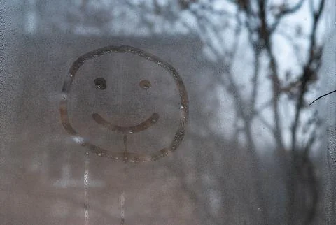 A painted smiling smiley face on a window with drops. The concept of happy .. Stock Photos