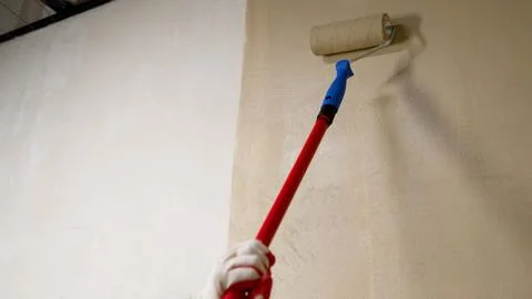 Painter applying beige paint with roller on white wall Stock Photos