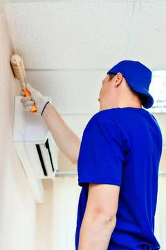 A painter in a cap and gloves paints the wall with a paint roller. Portrait of a Stock Photos
