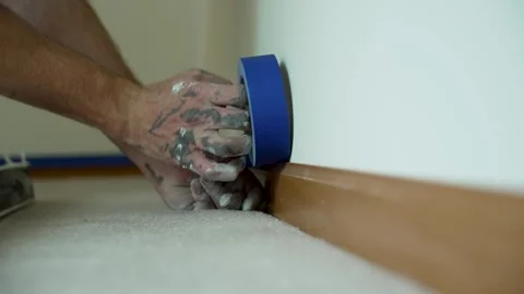 A painter carefully applies blue masking tape along the baseboard to ensure Stock Footage 324801167