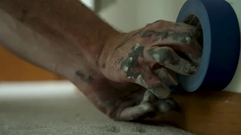 A painter carefully applies blue masking tape along the baseboard to ensure Stock Footage 324802507