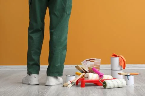 Painter in green uniform with renovation tools and color palette on wooden fl Stock Photos