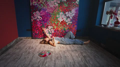 Painter lying on the floor admiring her floral artwork Stock Footage 307106144