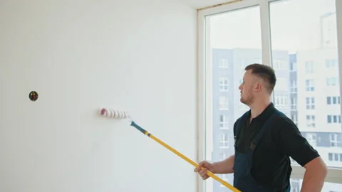 Painter man. A bearded construction worker in a blue overalls is painting a wall Stock Footage 232169072