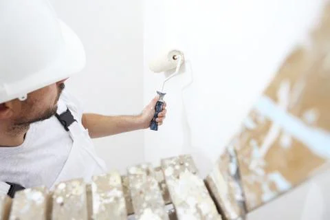 Painter man at work with a paint roller, on ladder, wall painting concept Stock Photos