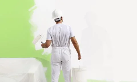 Painter man at work with a paint roller, wall painting green color ecological Stock-Fotos
