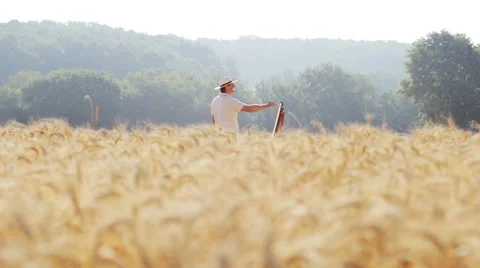 Painter in the middle of a wheat field paints a beautiful landscape, easel Stock Footage 28312658