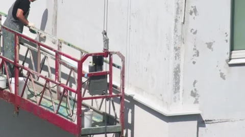 Painter In Overalls Works On Building Facade Renovation. Man Uses Paint Roller Stock Footage 322093322