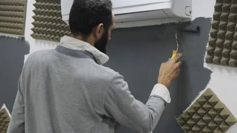 Painter painting studio wall between acoustic foam with grey paint using roll Stock Footage 220714400