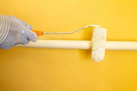A painter paints a pipe white with a roller, a gloved hand paints a pipe white Stock Photos