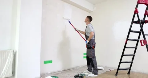 Painter paints wall of apartment with roller brush in white Stock Footage 259179349