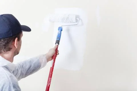 Painter paints wall with paint roller white 스톡 사진