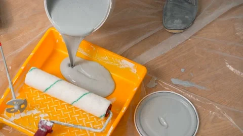 A painter pours gray paint from a bucket into a tray for further painting the Stock-Footage 151828150