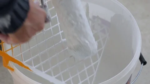The painter removes excess paint from the roller in a bucket of paint. Stock Footage 84887630