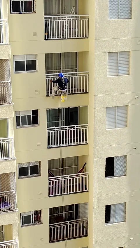 Painter in safety gear doing maintenance on a tall building's facade. Video stock 312897701