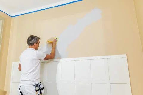 Painter sanding interior wall with hand sander during home renovation. Stock Photos