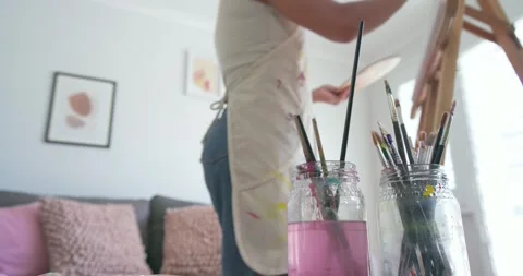 Painter shifting at easel reaching for brushes, rinsing in pink jar and applying 库存影片 344851395