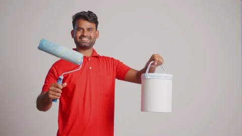 Painter showing roller paint brush with paint bucket by looking camera on white Video stock 233901221