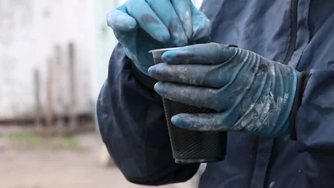 Painter stirs and mixes black paint in a glass in a dirty work uniform in paint Stock Footage 305258130