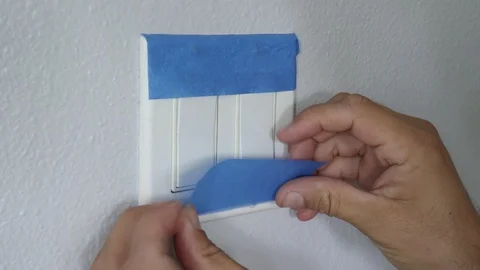 Painter Using Masking Blue Tape to Secure Light Switch. Preparation For Room Stock Footage 129138441