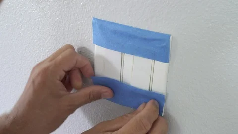 Painter Using Masking Blue Tape to Secure Light Switch. Preparation For Room Stock Footage 129138531
