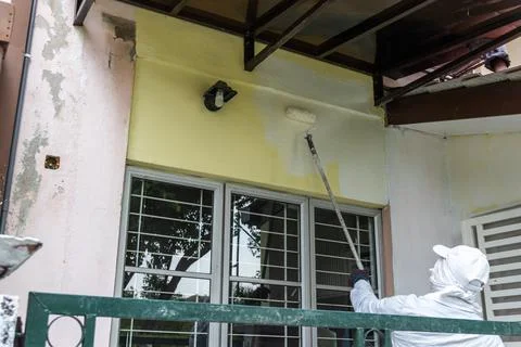 Painter worker adding undercoat foundation paint onto wall with roller at Stock Photos