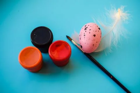 Painting Easter Egg with Brush and Paint Jars on Blue Background Stock Photos