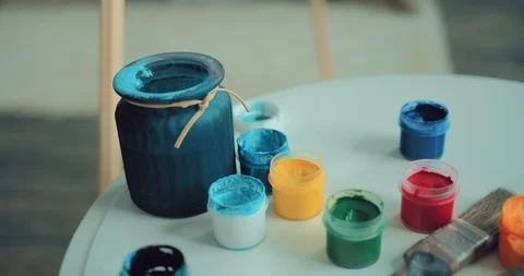 Paints in the jar are on the table, the brush is dipped in a jar of water Stock Footage 104576969