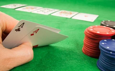 A pair of aces in a hand with a stack of chips and cards on table in the back Stock Photos