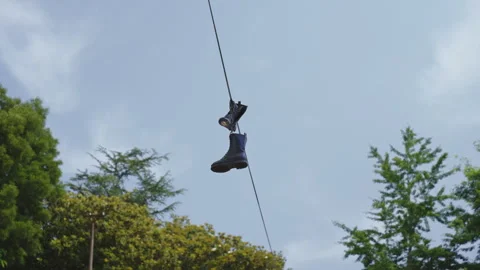 A pair of black boots dangling from an overhead wire against a soft, blue sky Stock Footage 336054408