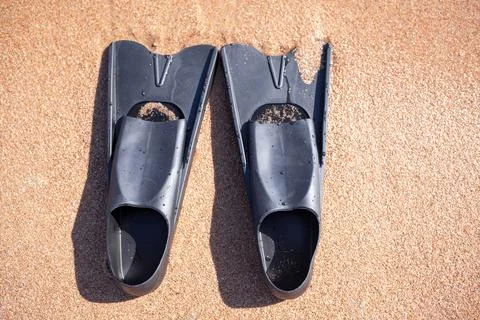 A pair of black flippers on the background of sand next to the water Foto stock
