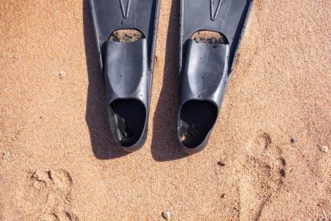A pair of black flippers on the background of sand next to the water Stock Photos