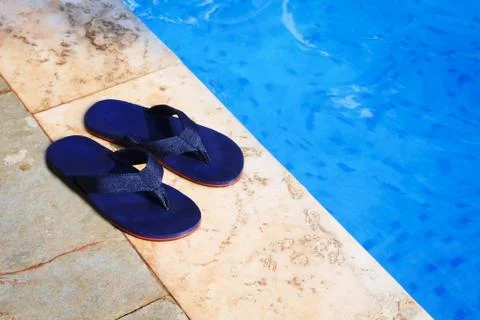 Pair of blue flip flops at the edge of a swimming pool Stock Photos
